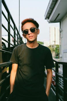 一个戴着墨镜的年轻人，随意地站在阳光明媚的户外城市环境中