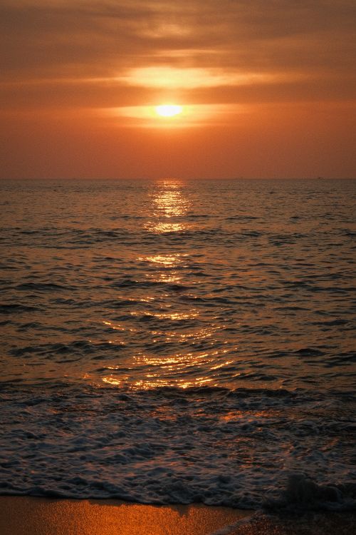 Free A beautiful sunset over calm ocean waves, with golden reflections on the water. Stock Photo