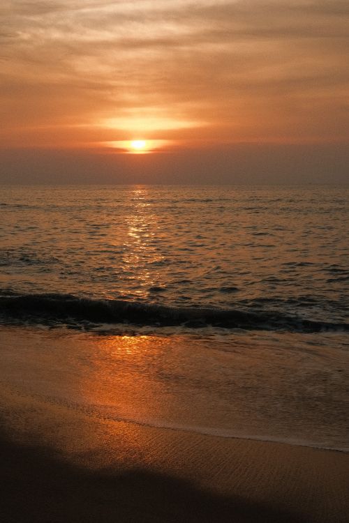 Free Beautiful sunset over a tranquil beach with calm ocean waves and a serene sky. Stock Photo
