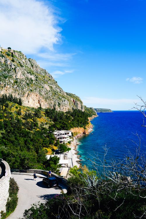 Free A breathtaking view of a coastal road alongside rocky cliffs and shimmering blue sea under a clear sky. Stock Photo