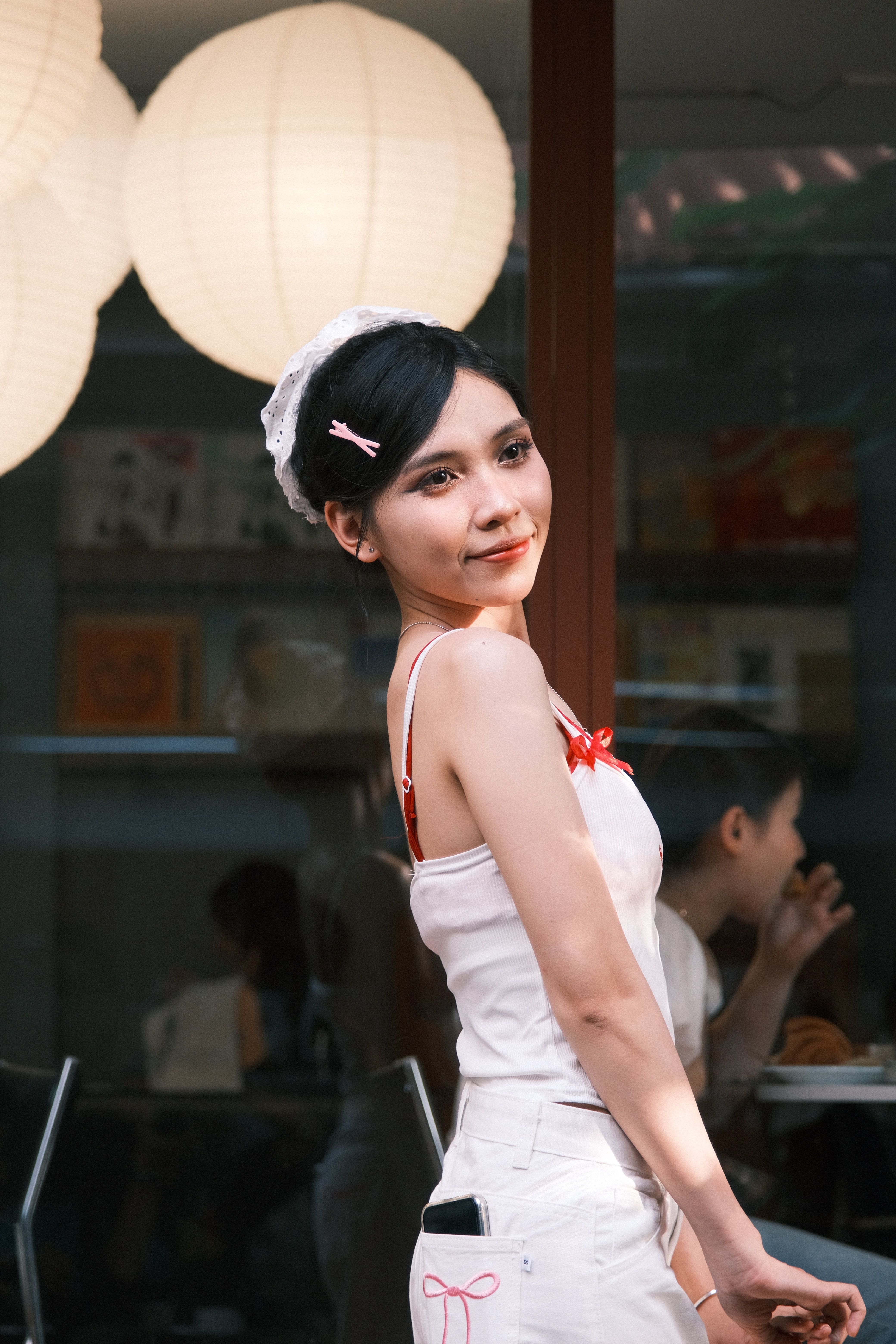 Elegant woman in white outfit poses confidently in a modern cafe with Asian influence.