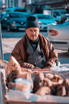 Elderly man selling produce on a busy city street, dressed warmly for winter.