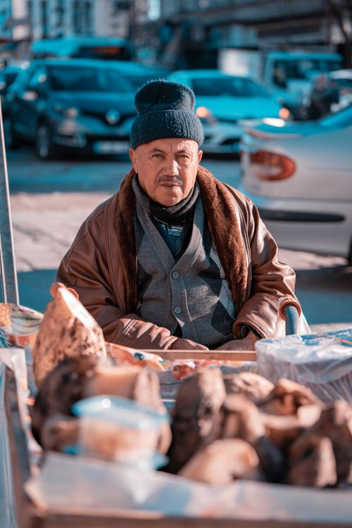 Free Elderly man selling produce on a busy city street, dressed warmly for winter. Stock Photo