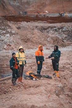 A group of construction workers warming themselves by a fire on a worksite.