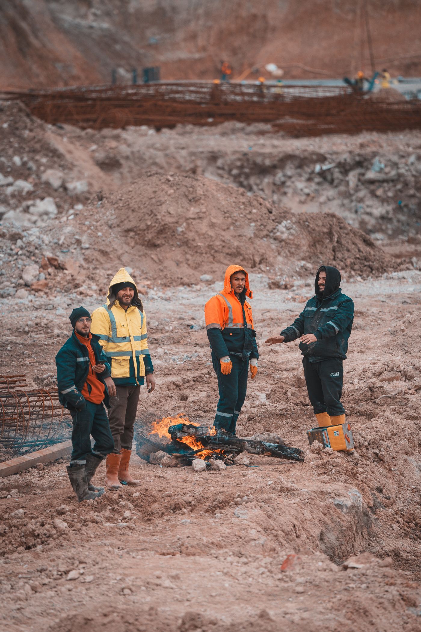 Four workers in winter work clothes warming up by a small fire on a building site
