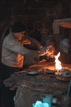 A man prepares traditional street food in a rustic setting with open fire cooking.