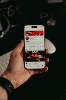 A hand holding a smartphone displaying a mobile app interface with dark, modern visuals.
