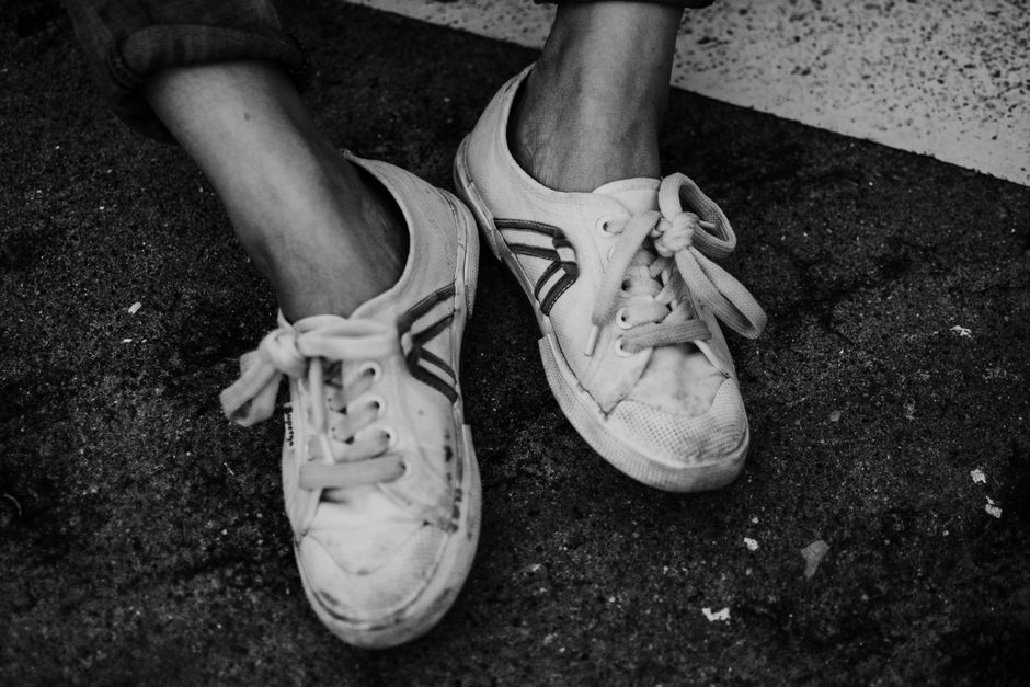 Black and white of pair of white dirty sneakers on legs of unrecognizable person placed on asphalt ground