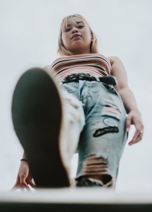 Low Angle Photo of Woman in Distress Denim Jeans Posing While Looking Down