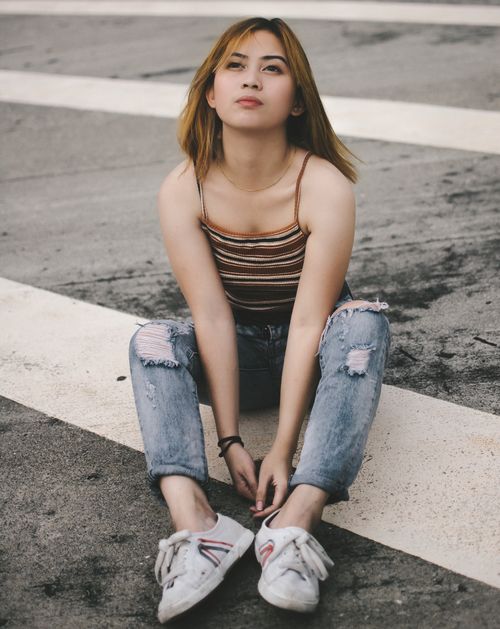 Free Casual fashion portrait of a young woman sitting on a city street. Stock Photo