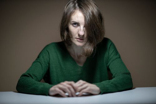 Free A contemplative woman in a green sweater sitting at a table, captured in a dimly lit indoor setting. Stock Photo