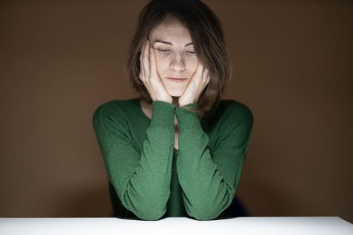 Free Thoughtful woman in green sweater looking down in low light setting. Stock Photo