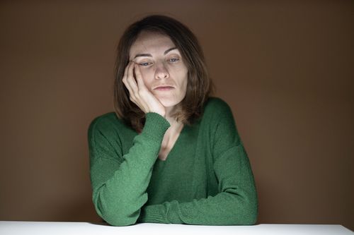 Free A thoughtful woman in a green sweater appears pensive, resting her head on her hand. Stock Photo