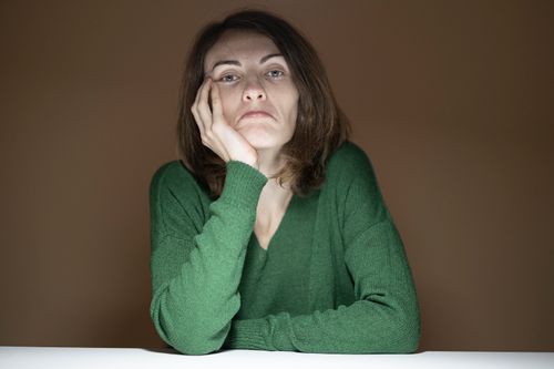 Free Thoughtful woman resting her face on hand in a green sweater indoors. Stock Photo