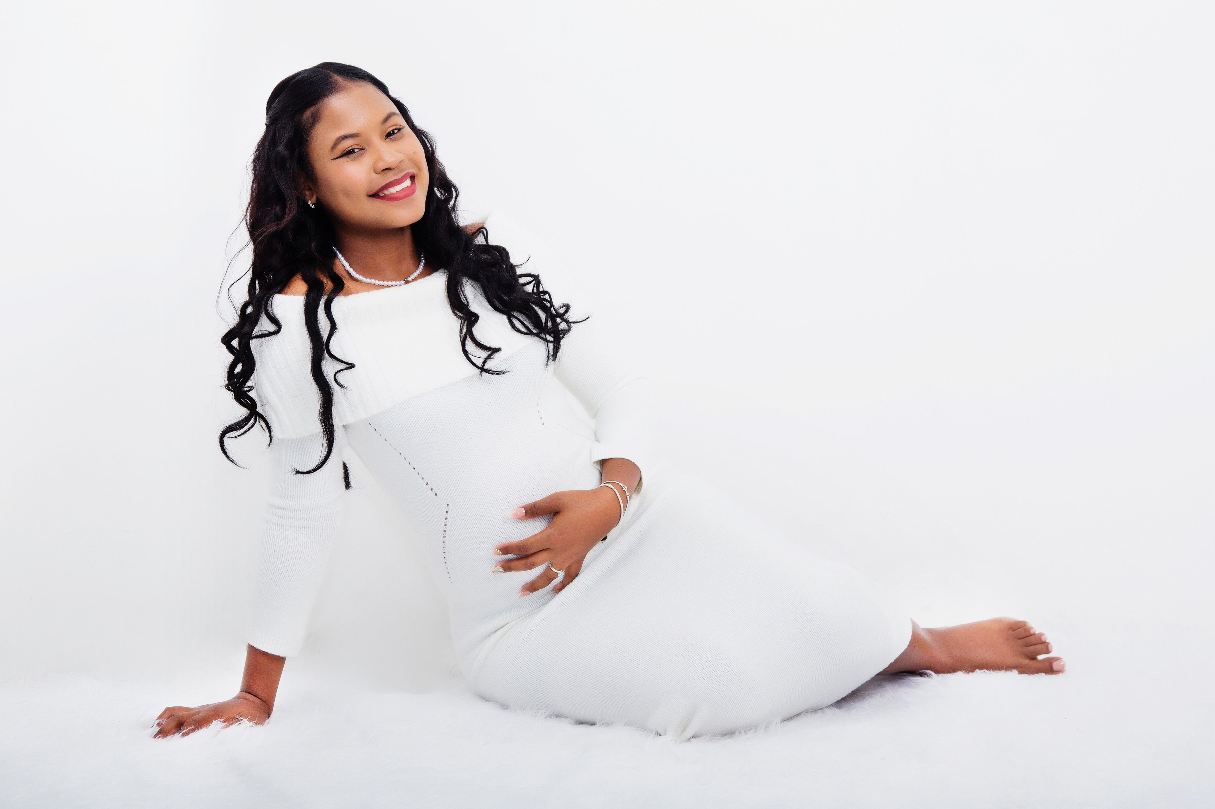 A beautiful, elegant maternity portrait showcasing a smiling woman in a white dress, set in a studio.