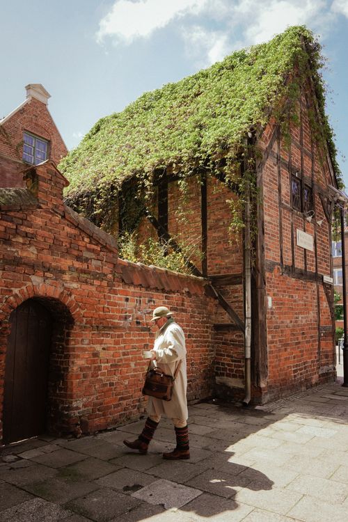 Free A man walks beside a historic ivy-covered brick building in sunlight. Stock Photo