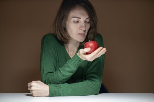 Free A thoughtful woman in a green sweater examines an apple indoors. Stock Photo