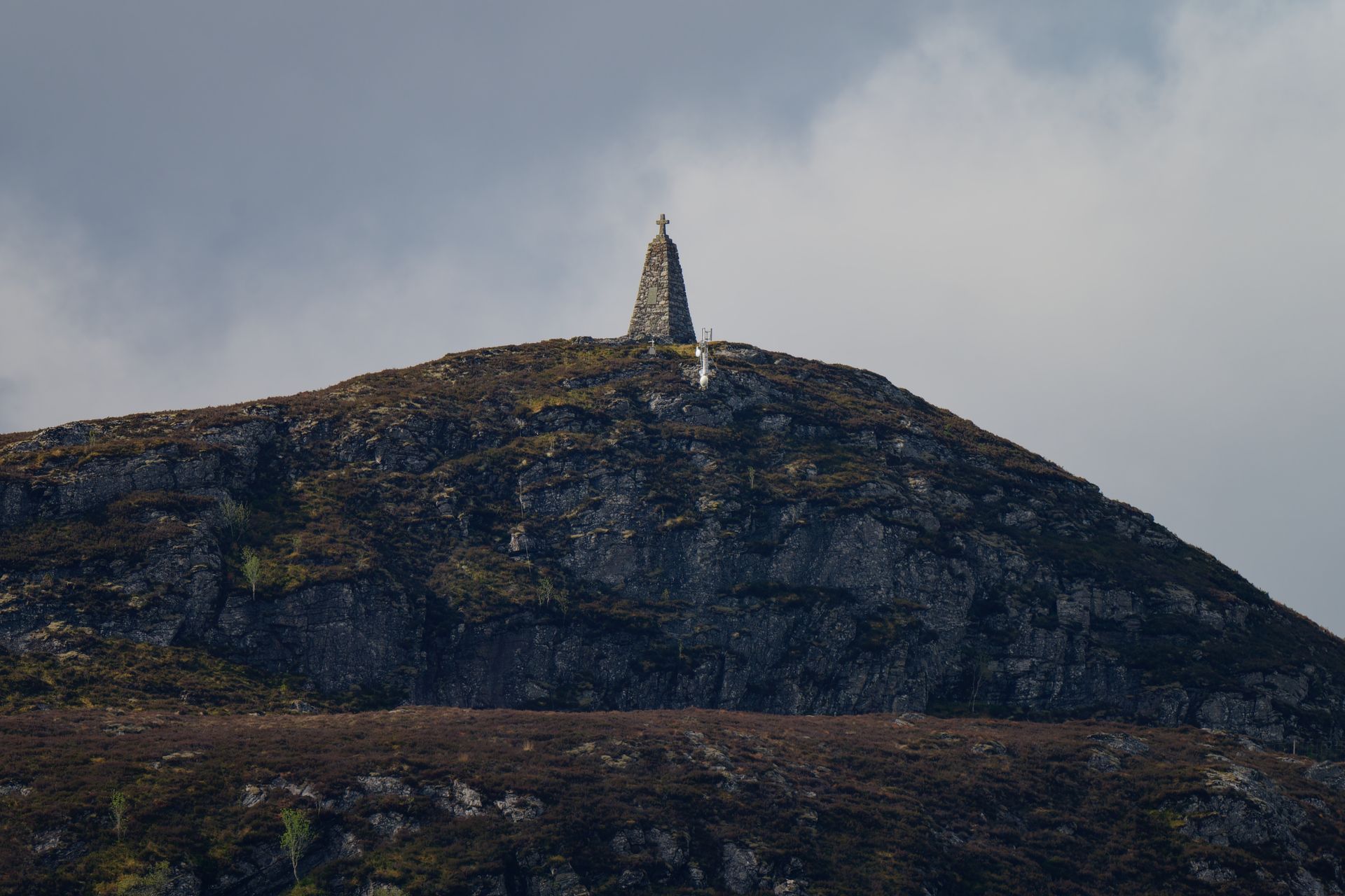 A stone cairn atop a rocky hill with a cloudy sky background, symbolizing solitude and serenity.