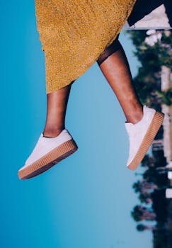 特写一个穿着黄色裙子和白色运动鞋的人，在晴朗的天空下于户外跳跃