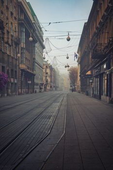 Foggy street scene with tram tracks in a historic European city.