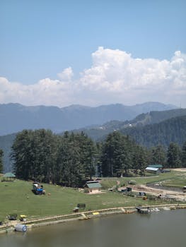 A scenic view of a tranquil lake surrounded by lush forests and distant mountains under a clear sky.