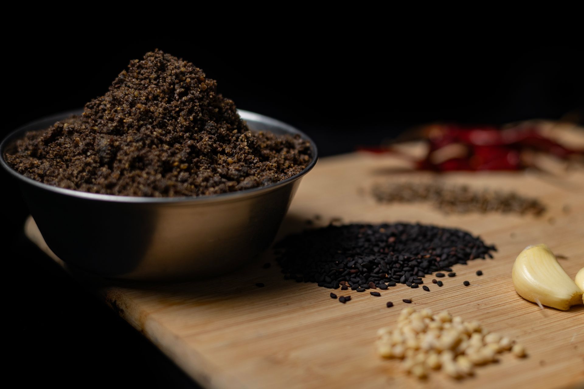 Close-up of assorted spices including black sesame and garlic on a wooden board.