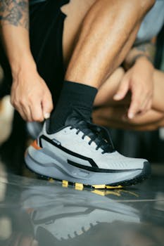 Close-up of a man tying a modern athletic shoe on a reflective surface indoors.