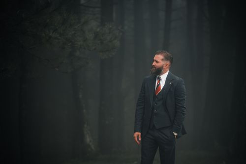 Free Confident man in a suit stands in a dark, misty forest. Eerie yet professional ambiance. Stock Photo