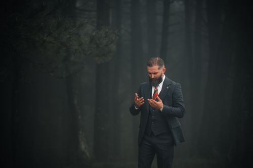 Free A businessman in a suit praying with a misty forest background. Stock Photo