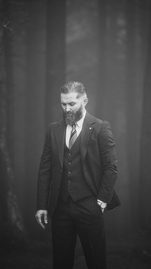 Free A contemplative man in a suit stands amidst a misty forest setting, captured in black and white. Stock Photo