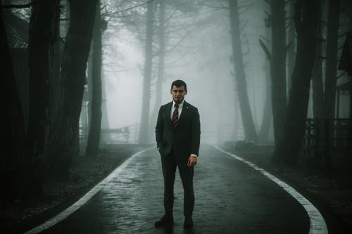 Free A solitary man in a suit stands on a foggy forest road, creating a moody atmosphere. Stock Photo