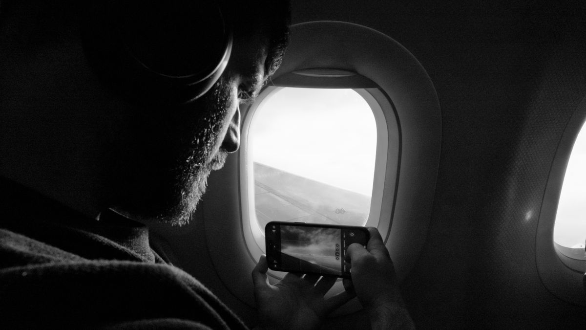 Man taking photo out of airplane window, capturing wing view with smartphone.