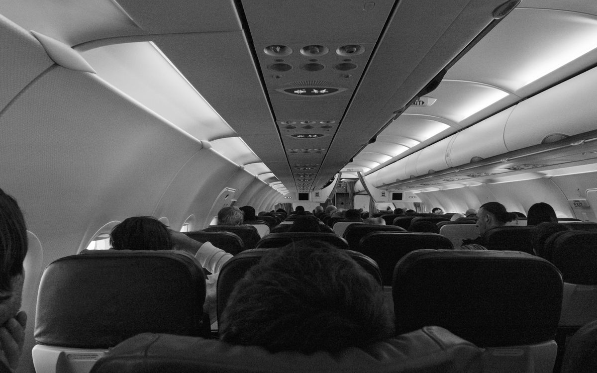 Black and white view of passengers seated inside an airplane cabin.