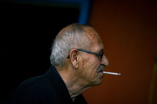 Free Close-up of an elderly man smoking a cigarette against a dark background. Stock Photo