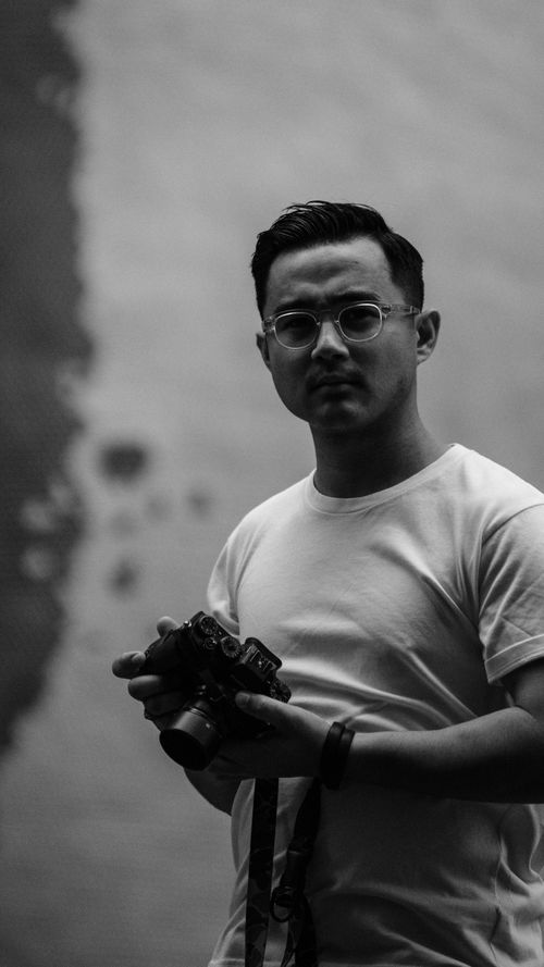 Free Black and white portrait of a man holding a camera, exuding a classic and moody atmosphere. Stock Photo