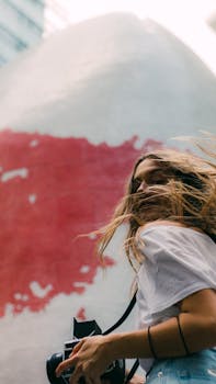 一个年轻女子在大风天带着相机，捕捉户外的城市场景