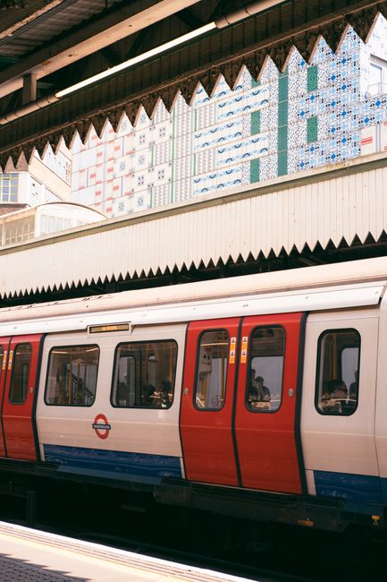 A London Underground train at a station with architectural details, surrounded by city buildings.