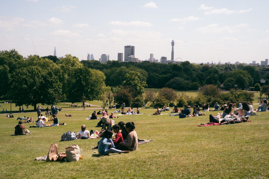 People relaxing on Primrose Hill with a view of the London skyline on a sunny day.