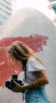 一位女士穿着休闲服装，手持相机探索城市艺术，背景是一面红色马赛克墙