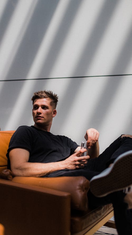 Photo of Man in Black Outfit Sitting on Brown Sofa While Looking Away