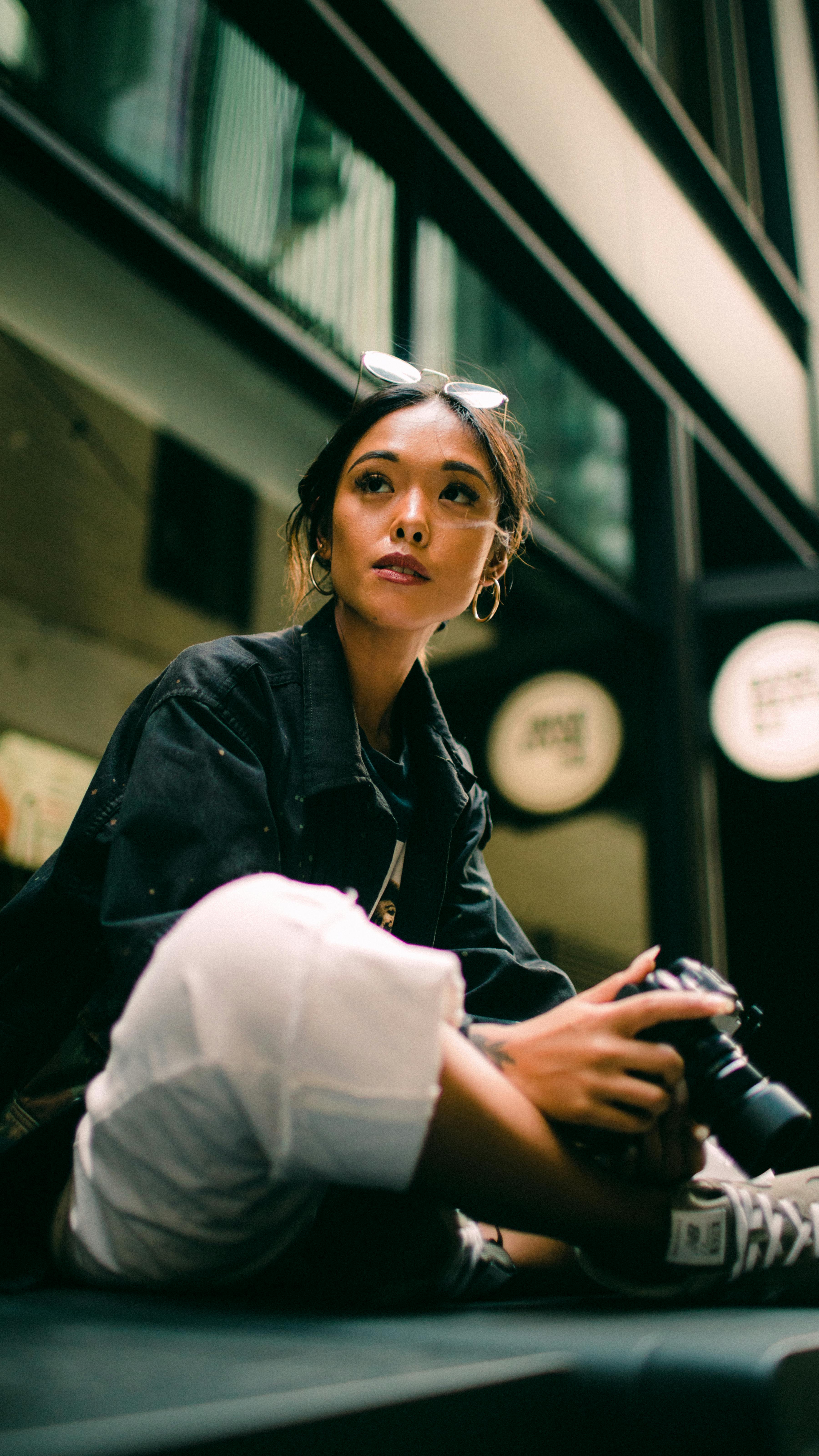 一位时尚女性坐在室内，手持相机，散发着休闲的优雅与创造力