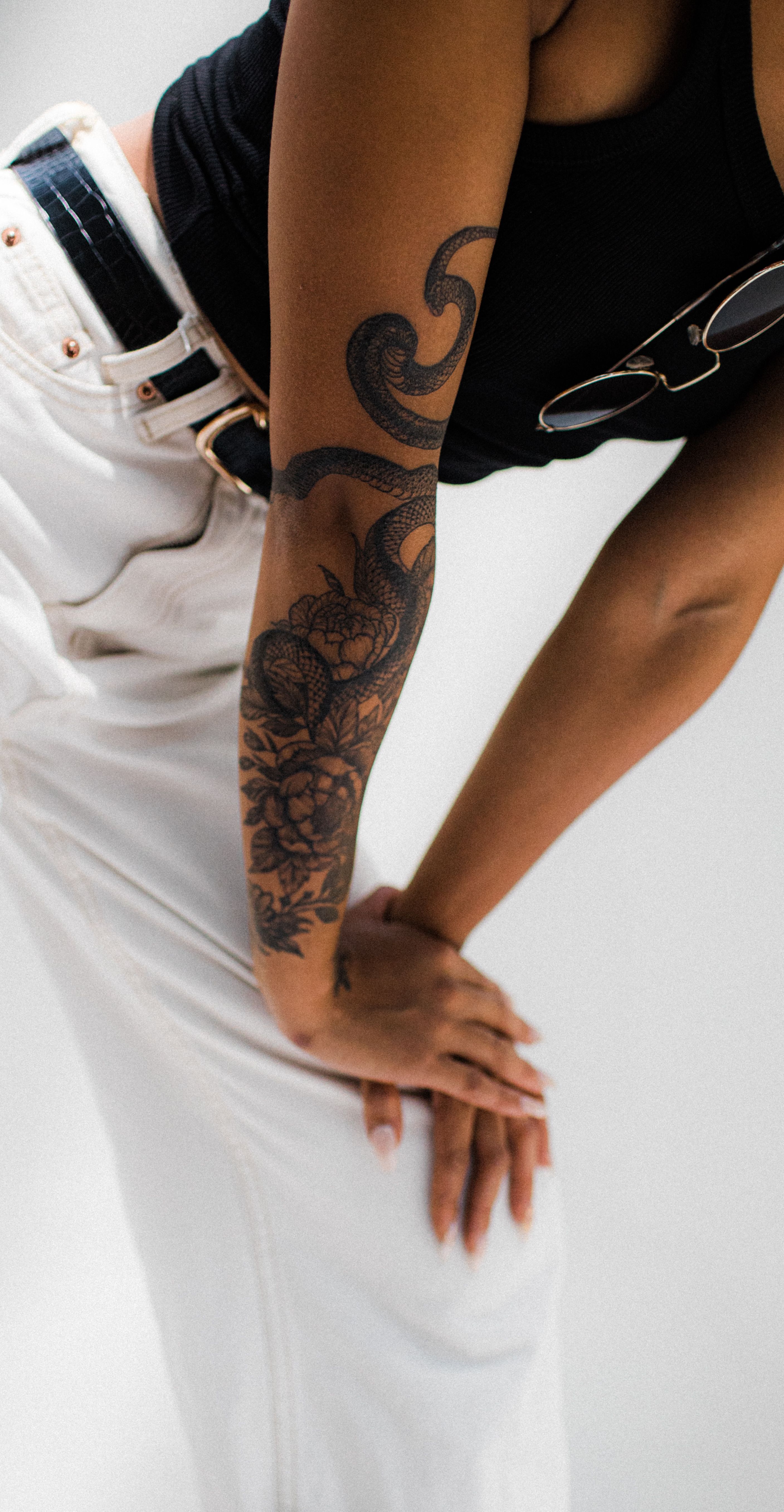 Stylish woman posing with floral arm tattoo and sunglasses indoors.