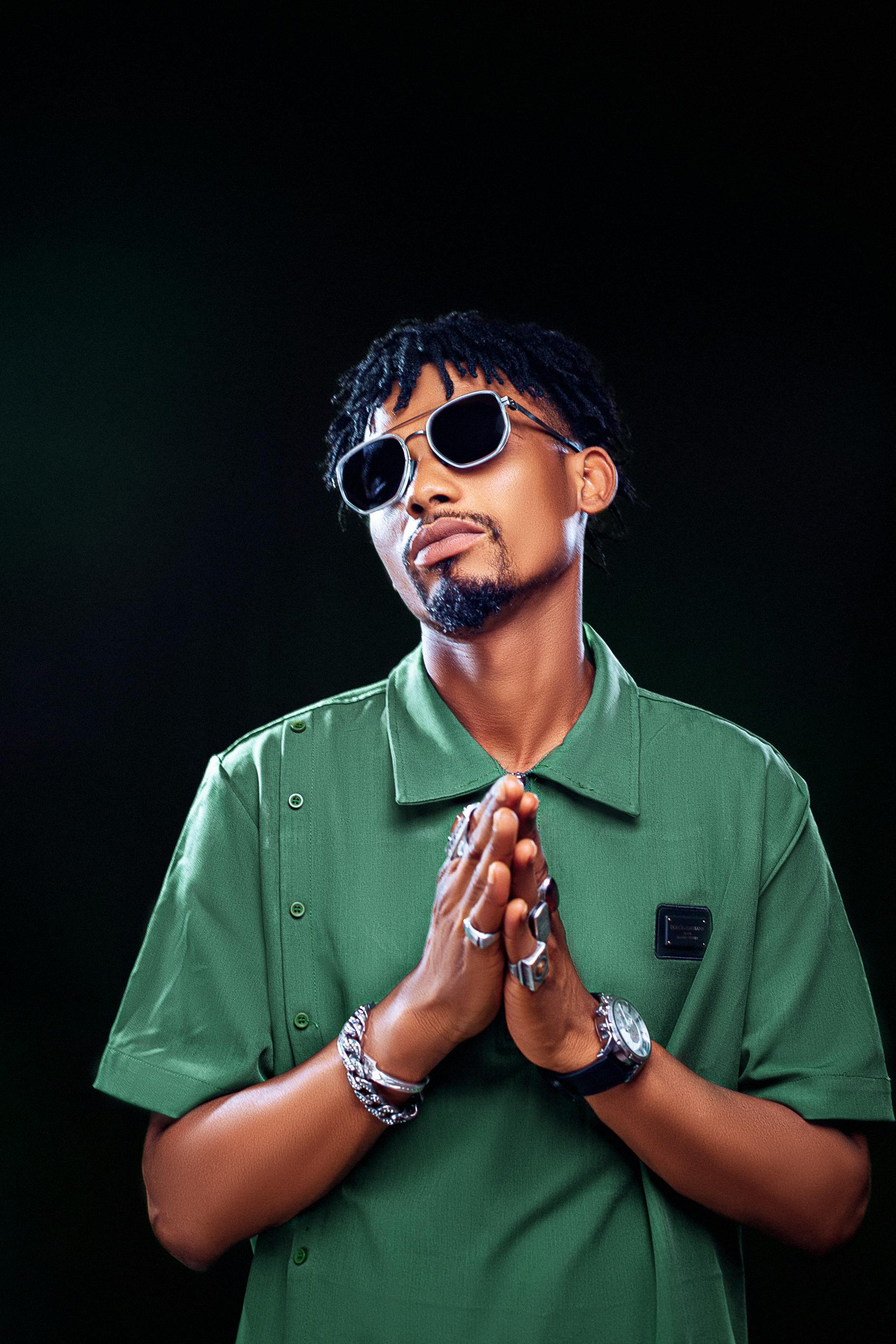 Portrait of a man with afro hair and sunglasses, wearing green in a studio setting.