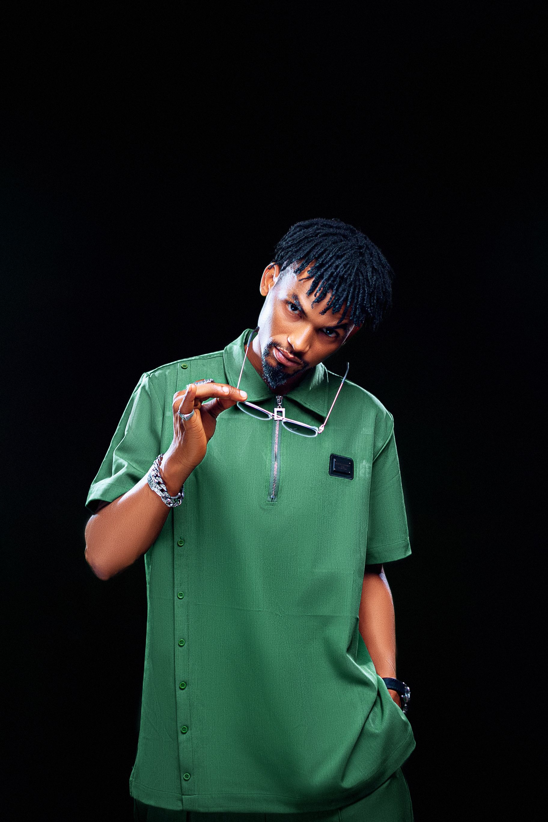 Portrait of a stylish man wearing a green shirt, striking a pose in a studio with a black background.