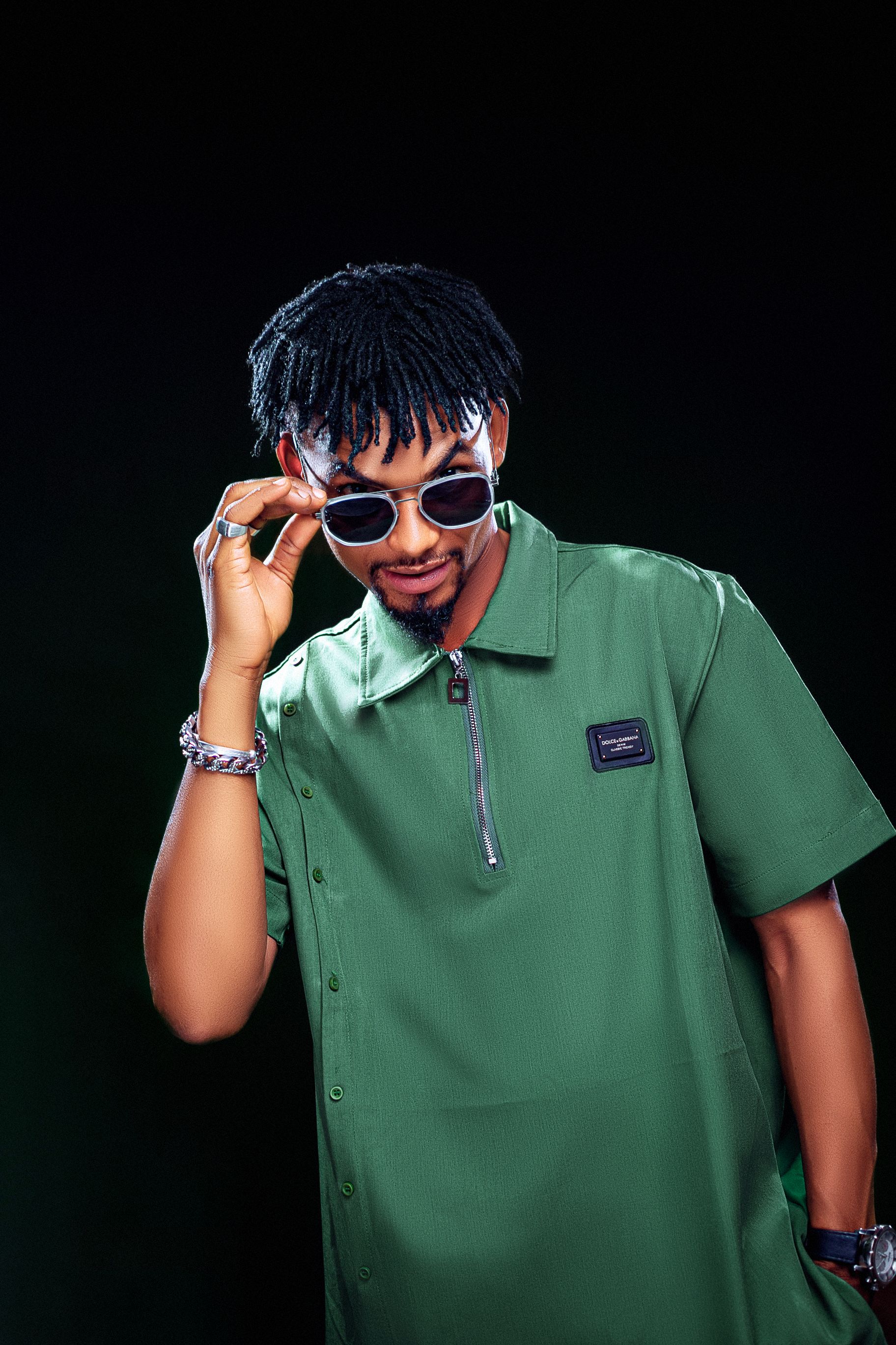Fashionable young man with afro hairstyle and sunglasses posing confidently in a studio.