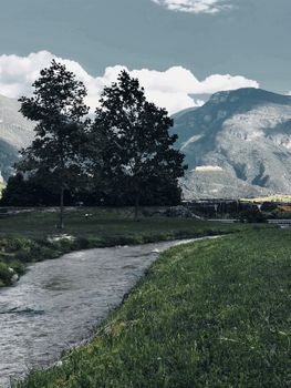 A tranquil mountain stream winding through a lush valley beneath towering peaks, creating a peaceful natural scene.