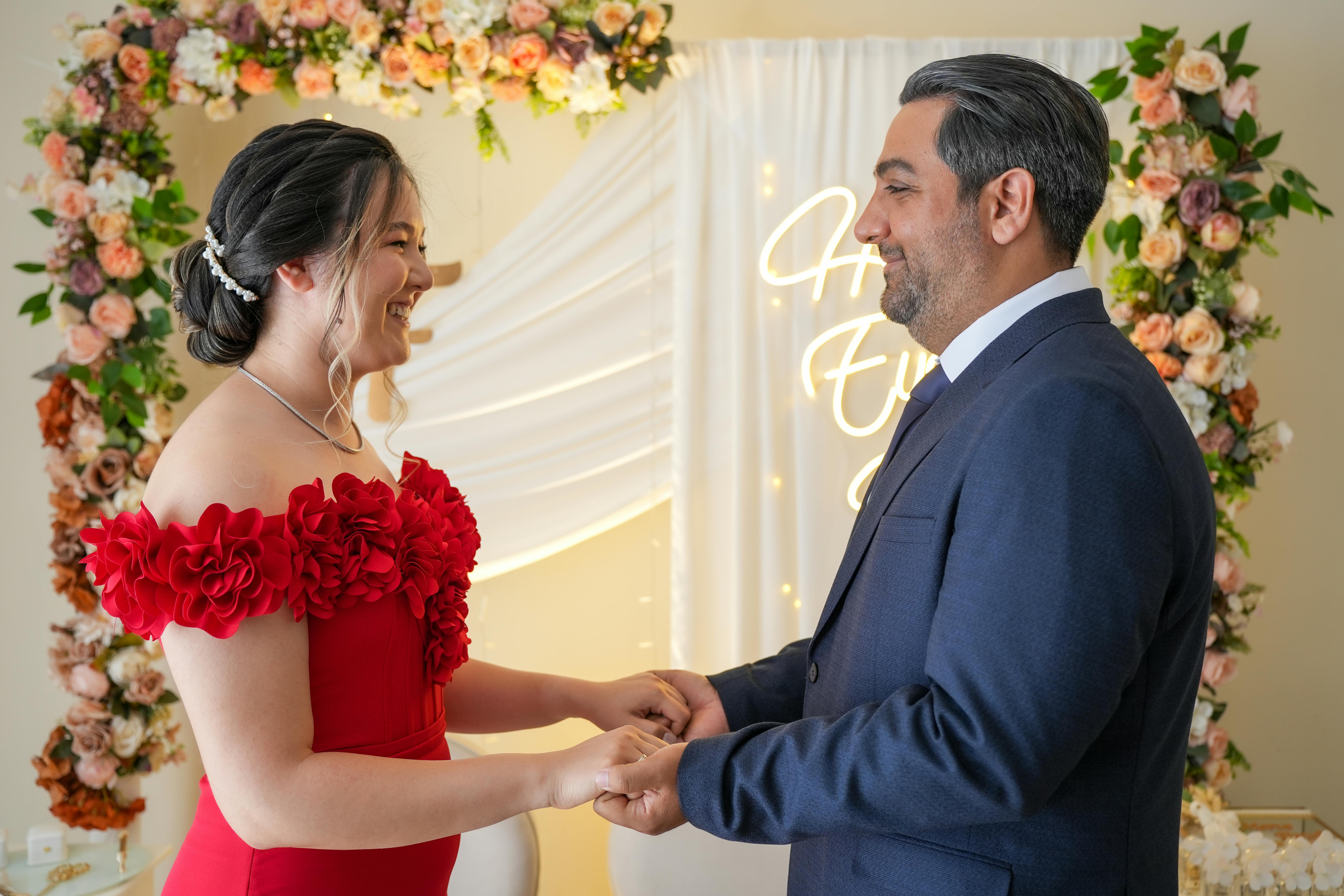 A couple joyfully exchanging vows under a beautiful floral arch indoors.