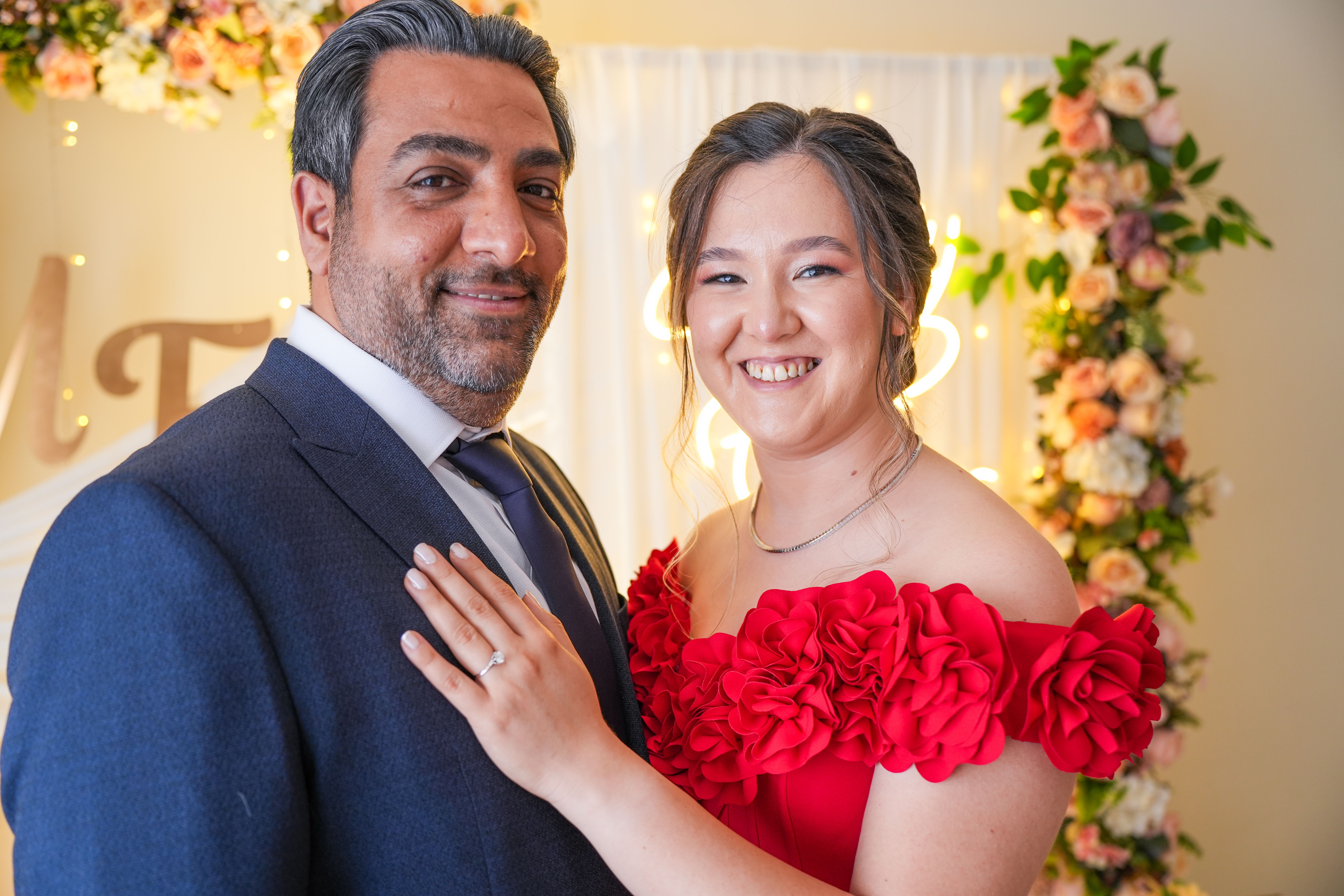 Happy couple celebrating engagement with elegant floral decor and warm lighting.