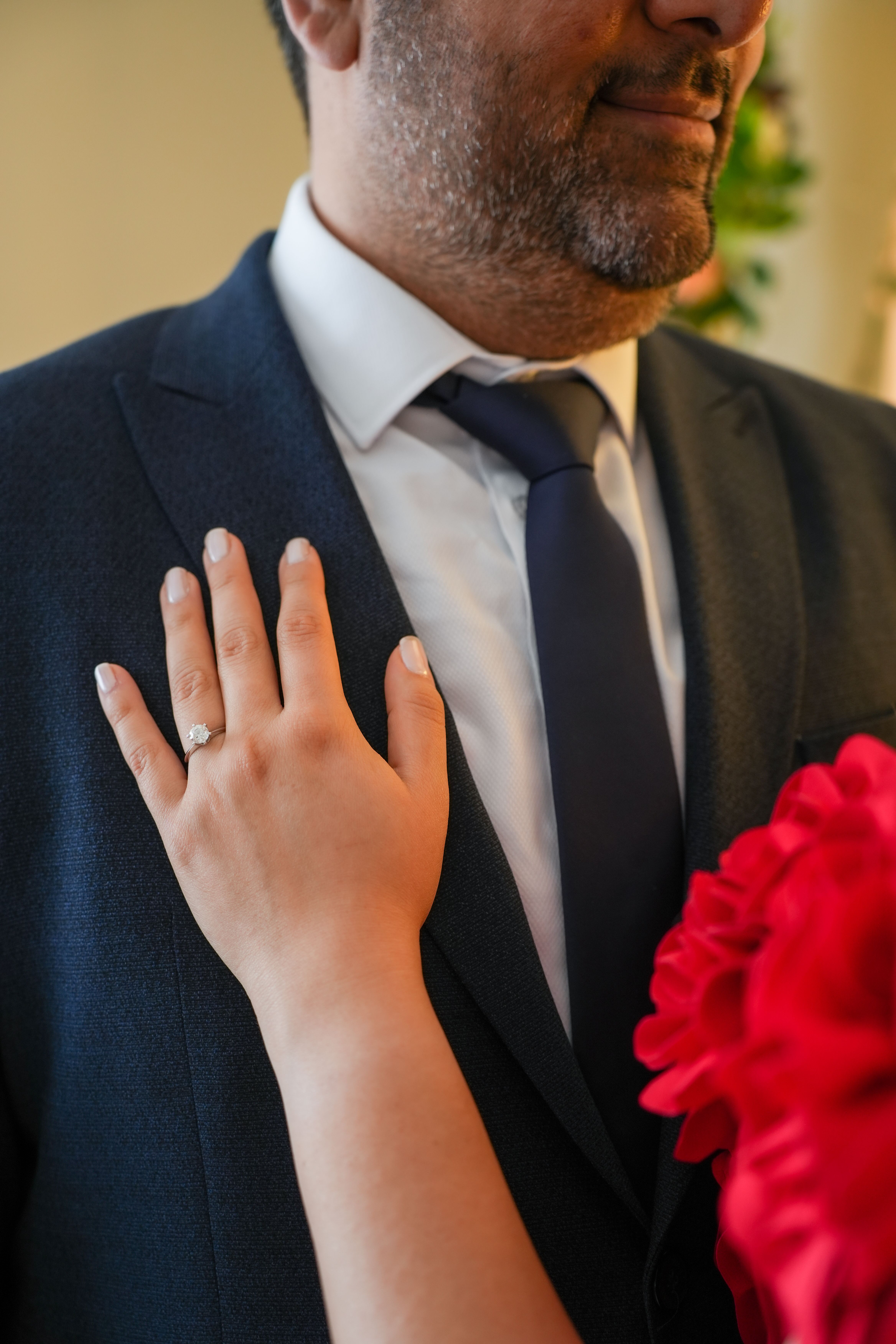 Close-up of hand with engagement ring resting on a navy suit jacket.