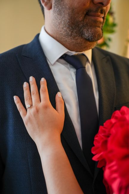 Close-up of hand with engagement ring resting on a navy suit jacket.